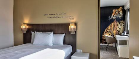 Una habitación de hotel con una cama, una mesita de noche, una silla, un escritorio y un mural de tigre en la pared.