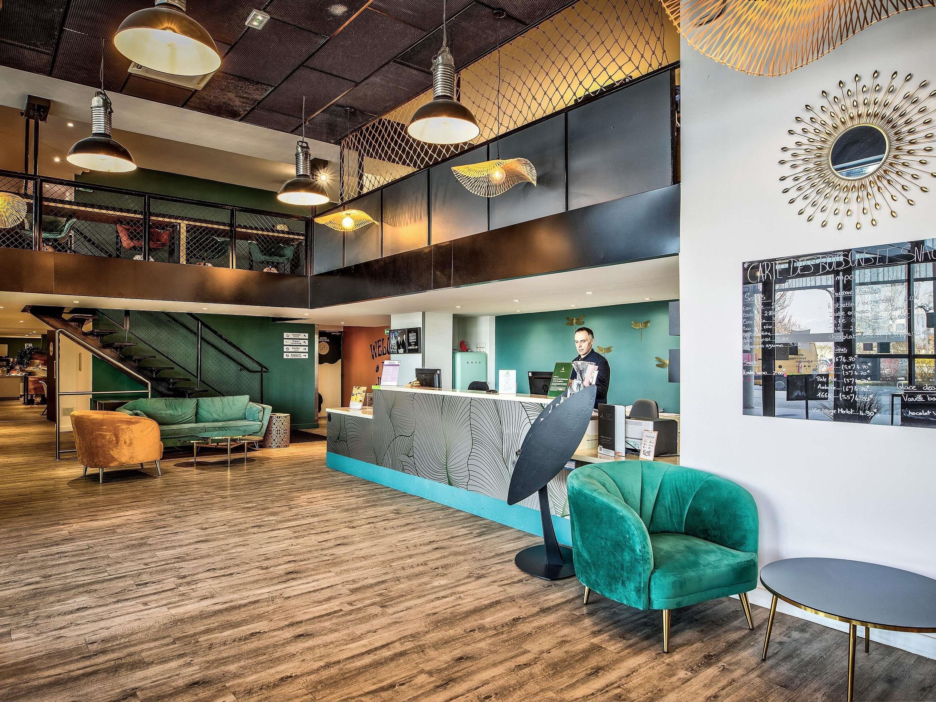 A modern interior with a reception desk, green seating, and a staircase.