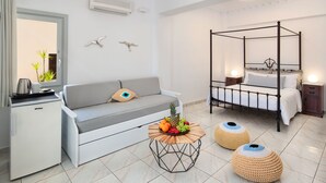 Un dormitorio moderno con cama con dosel, un sofá, una kitchenette pequeña y un frutero sobre una mesa redonda.