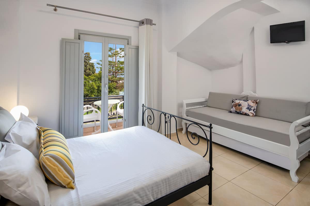 A bedroom with a bed, a sofa, a TV, and a balcony with outdoor furniture.