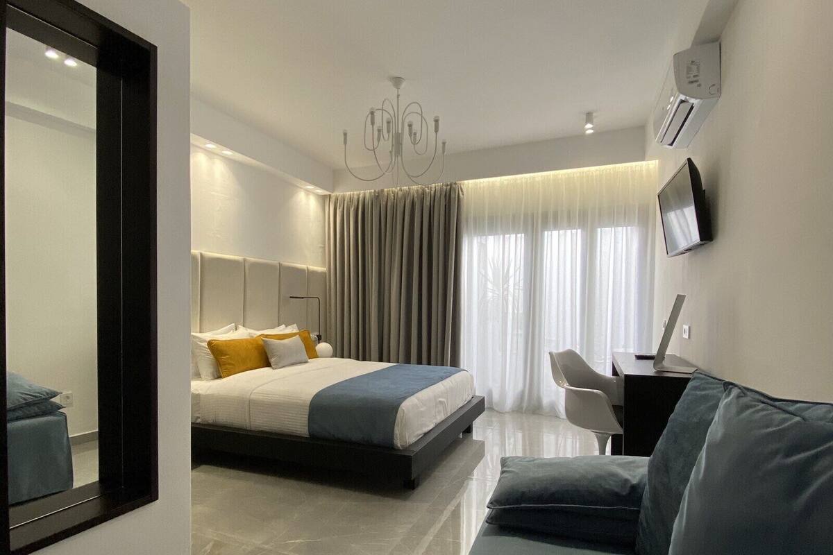 A modern hotel room with a bed, a sofa, a TV, and a large mirror.