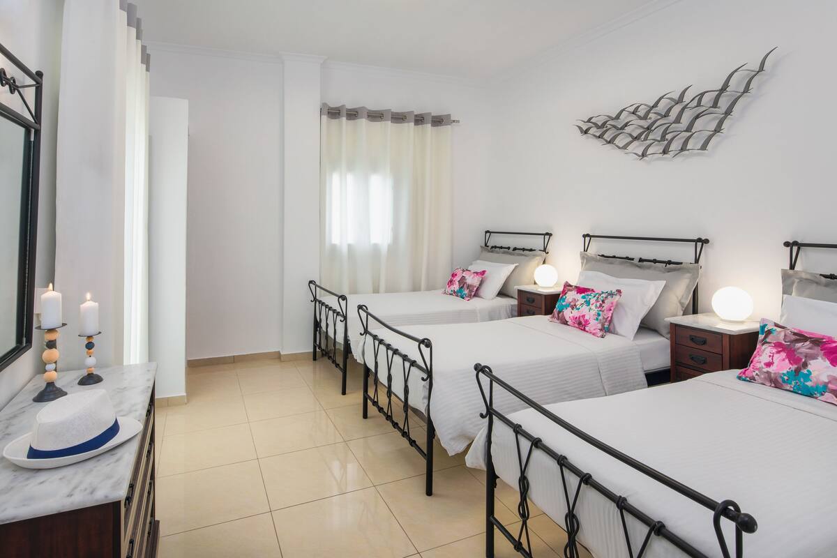 A hotel room with two beds, a marble bedside table, a mirror, a wall-mounted light fixture, and a decorative wall piece.