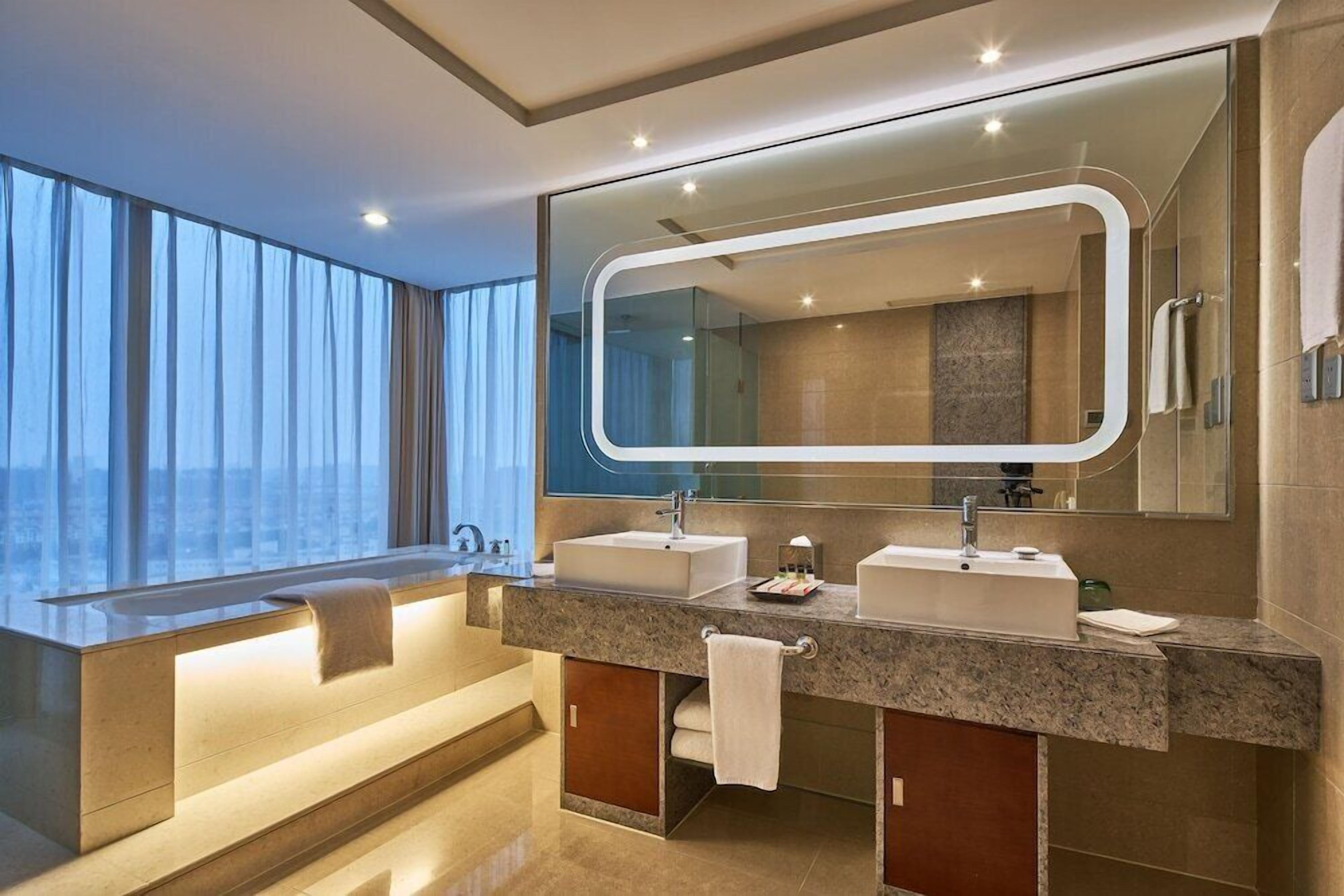 A modern bathroom with a large mirror, two sinks, and a bathtub.