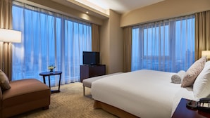 A hotel room with a large bed, a TV on a stand, a small table with a vase, and a view of the city through sheer curtains. - The Qube Hotel (Shanghai)
