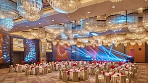 A banquet hall with multiple round tables, each set with white tablecloths and red centerpieces, surrounded by chairs. - The Qube Hotel (Shanghai)