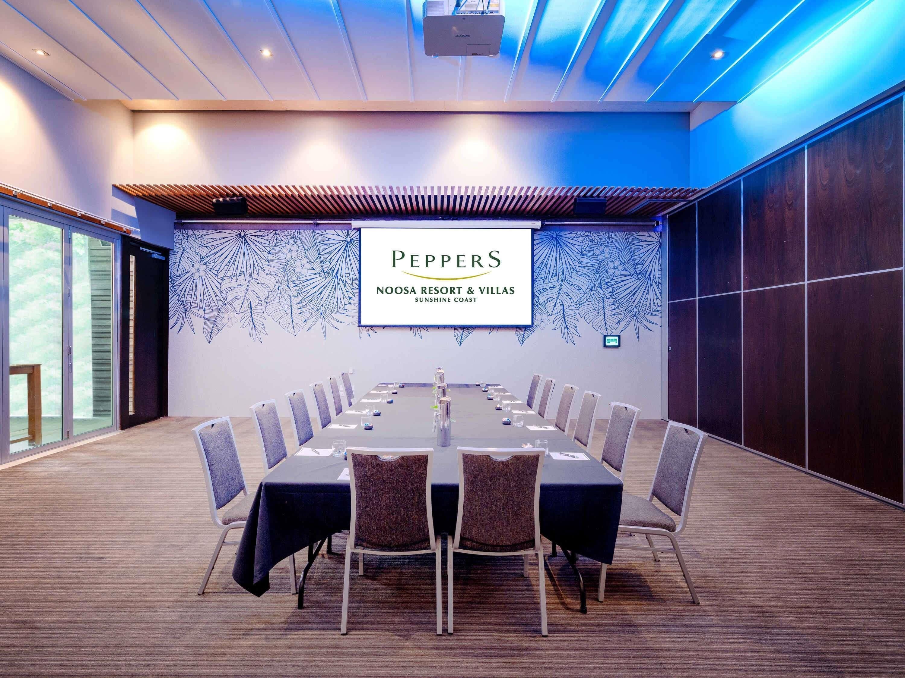 A conference room with a long table, chairs, and a projector screen displaying 'Peppers Noosa Resort & Villas Sunshine Coast'.