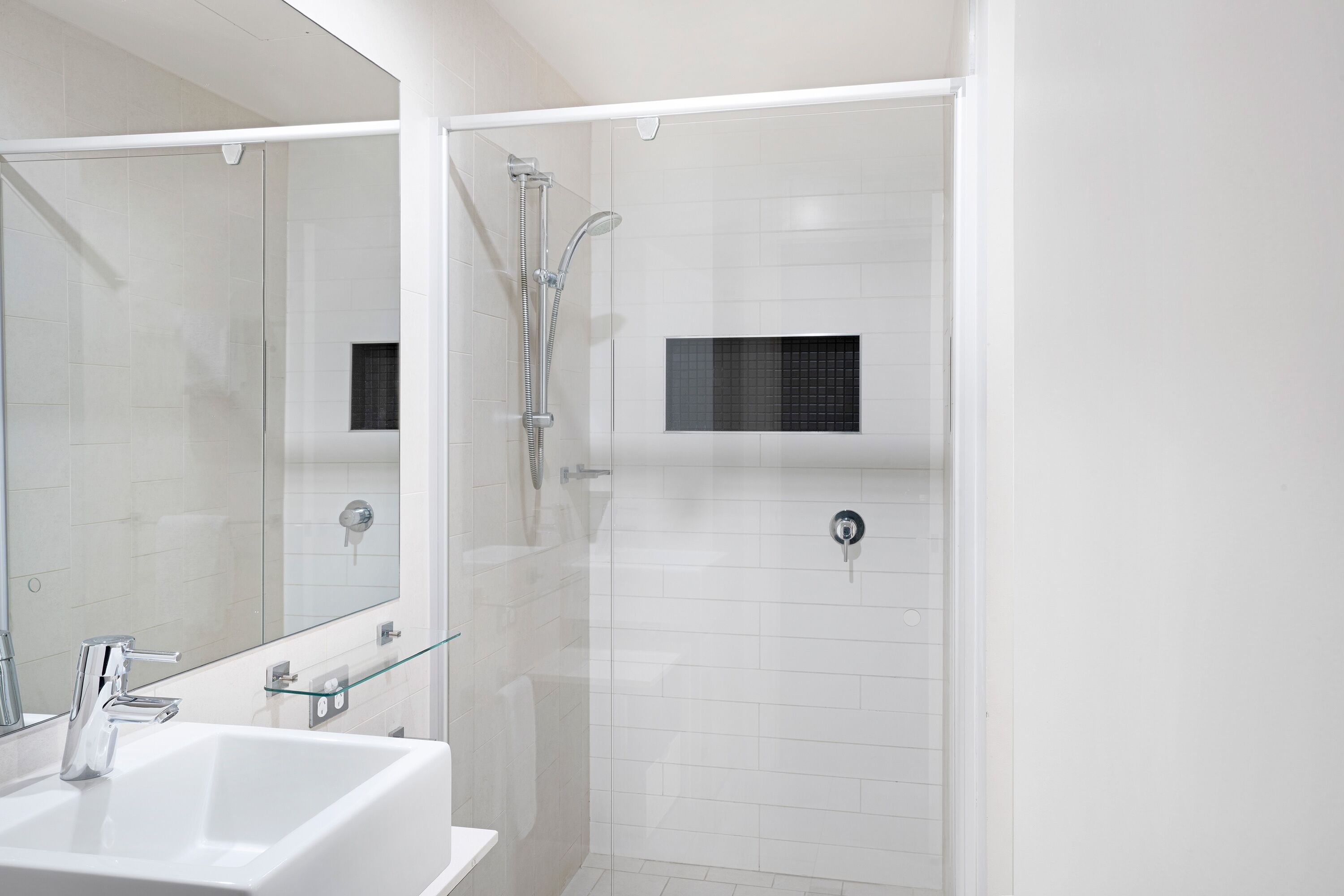 A modern bathroom with a glass shower enclosure, a white sink, and a large mirror.
