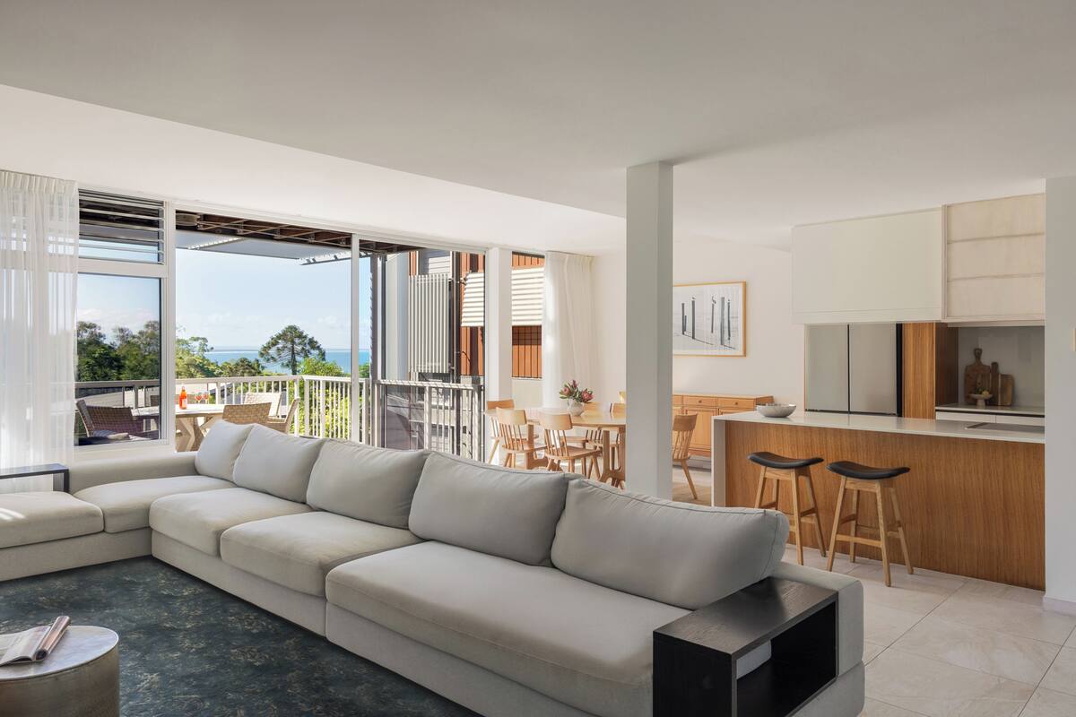 A modern living room with a large sofa, a dining area, and a kitchen with bar stools.