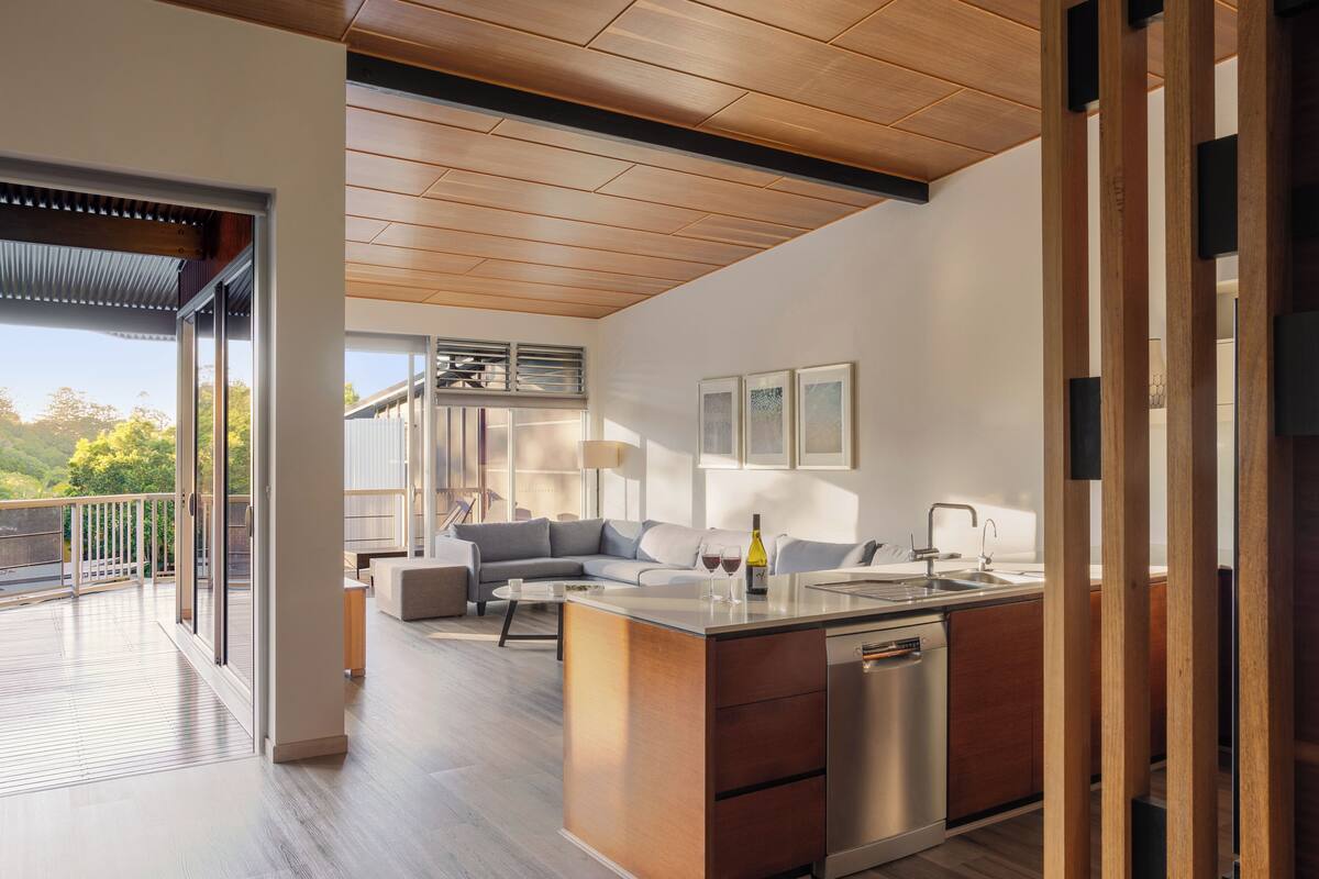 A modern kitchen with a built-in dishwasher, a dining area with a sofa, and a balcony with a railing.
