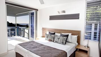 A bedroom with a large bed, a nightstand, a ceiling fan, and a view of the outdoors.