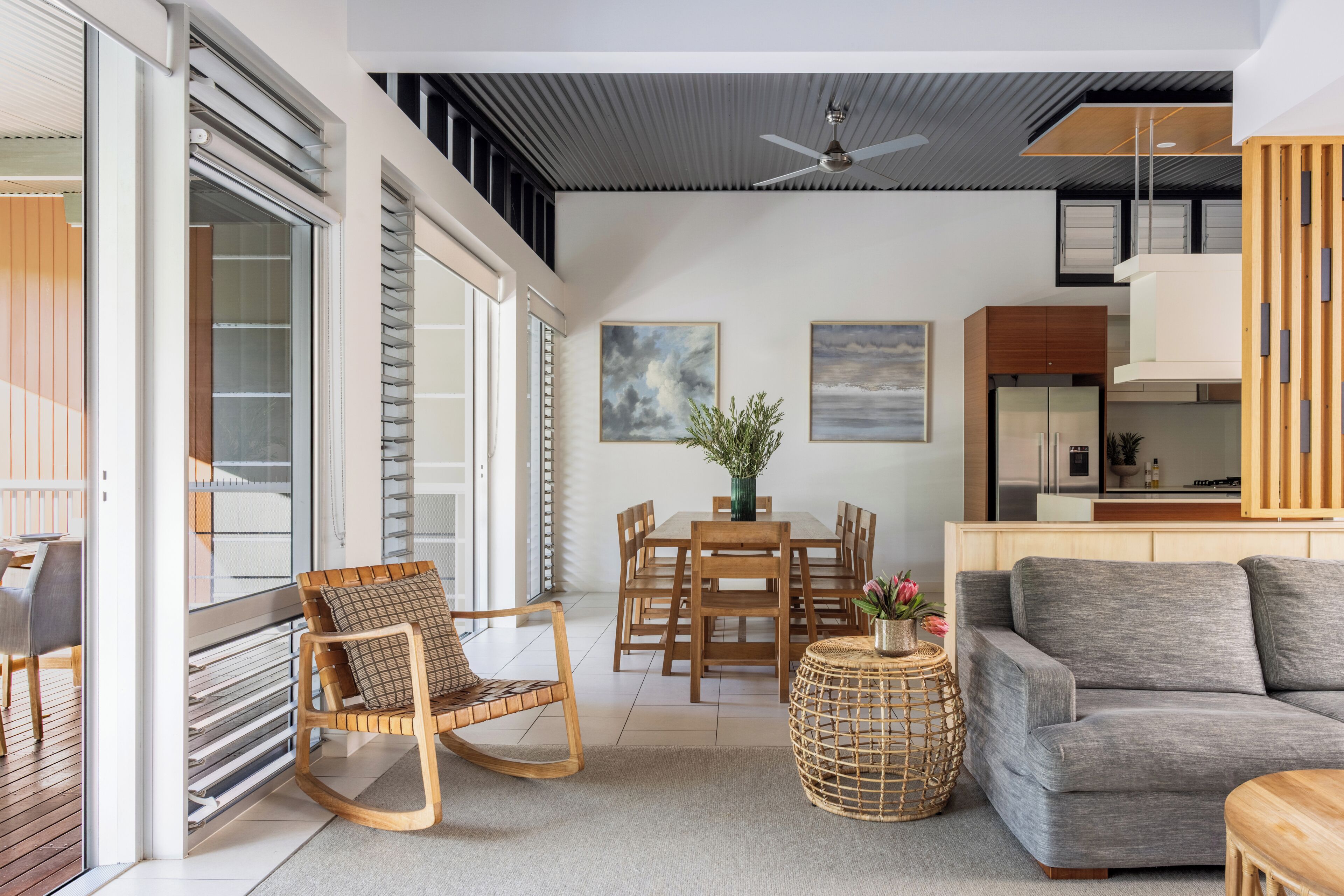 A modern living room with a dining area, a grey sofa, wooden furniture, and a ceiling fan.