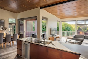 A modern kitchen with a built-in dishwasher, a dining area with chairs, a sofa, and a TV.