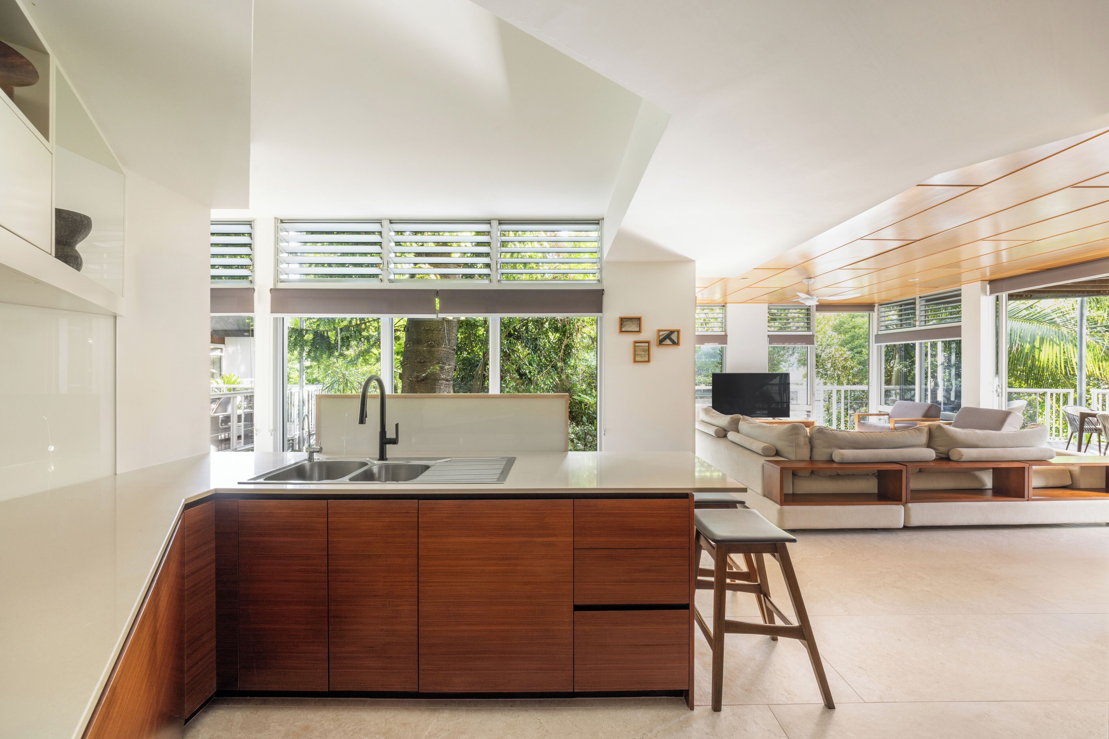 A modern kitchen with a large island, built-in wooden cabinets, and a large window overlooking greenery.
