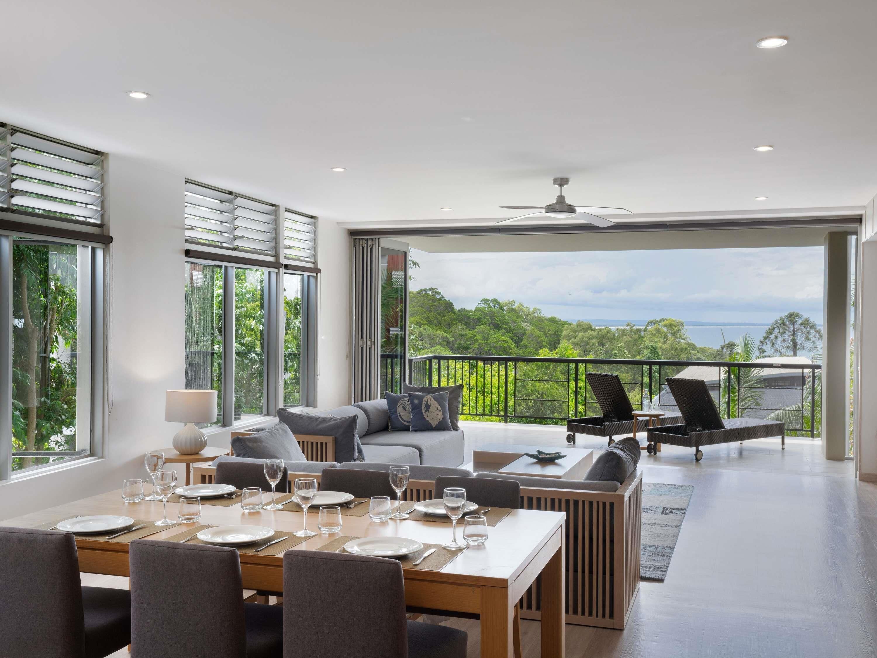 A modern dining area with a view of the outdoors, a balcony with outdoor furniture, and a ceiling fan.