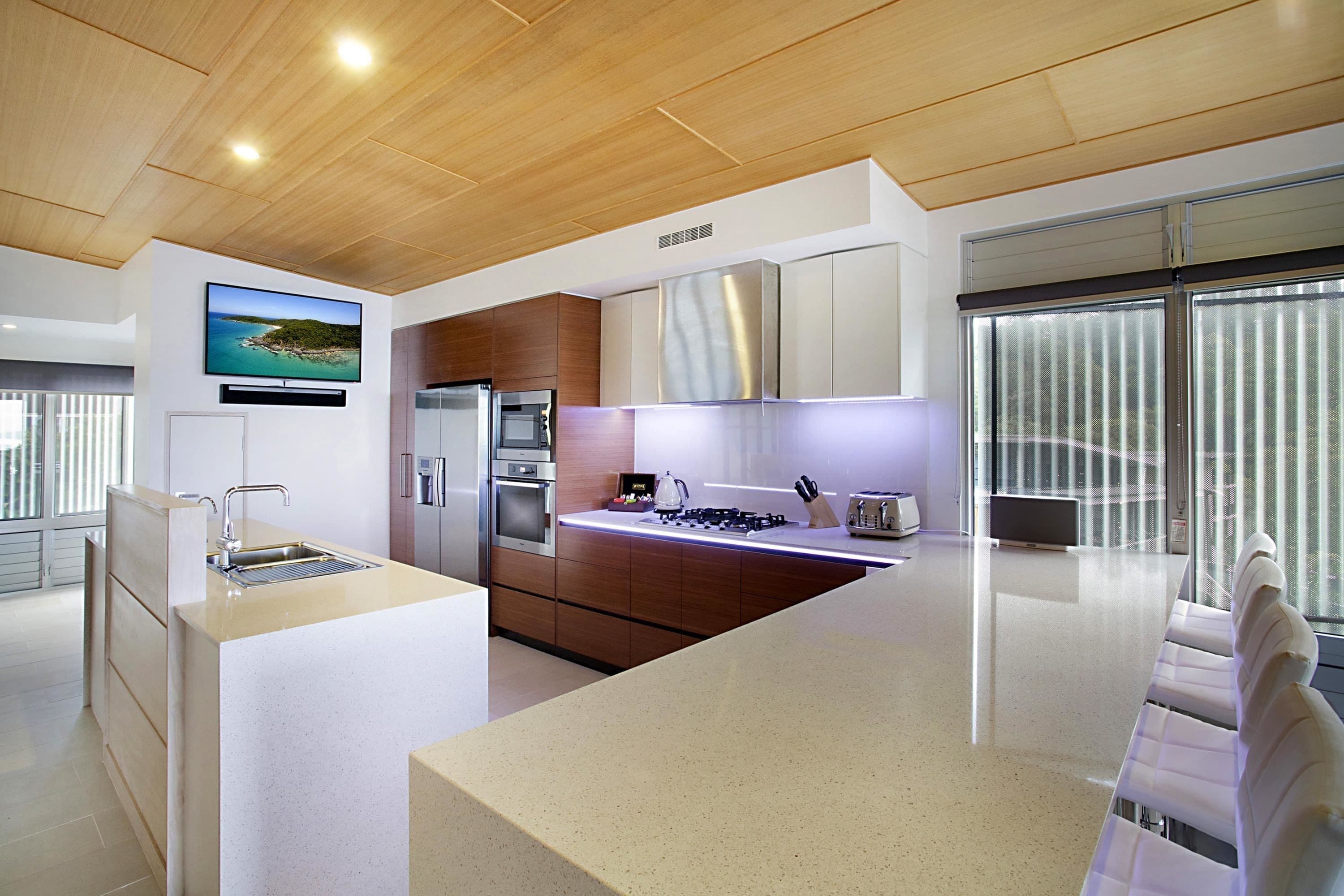 Una cocina moderna con una isla grande, electrodomésticos de acero inoxidable y un televisor de pantalla plana en la pared.