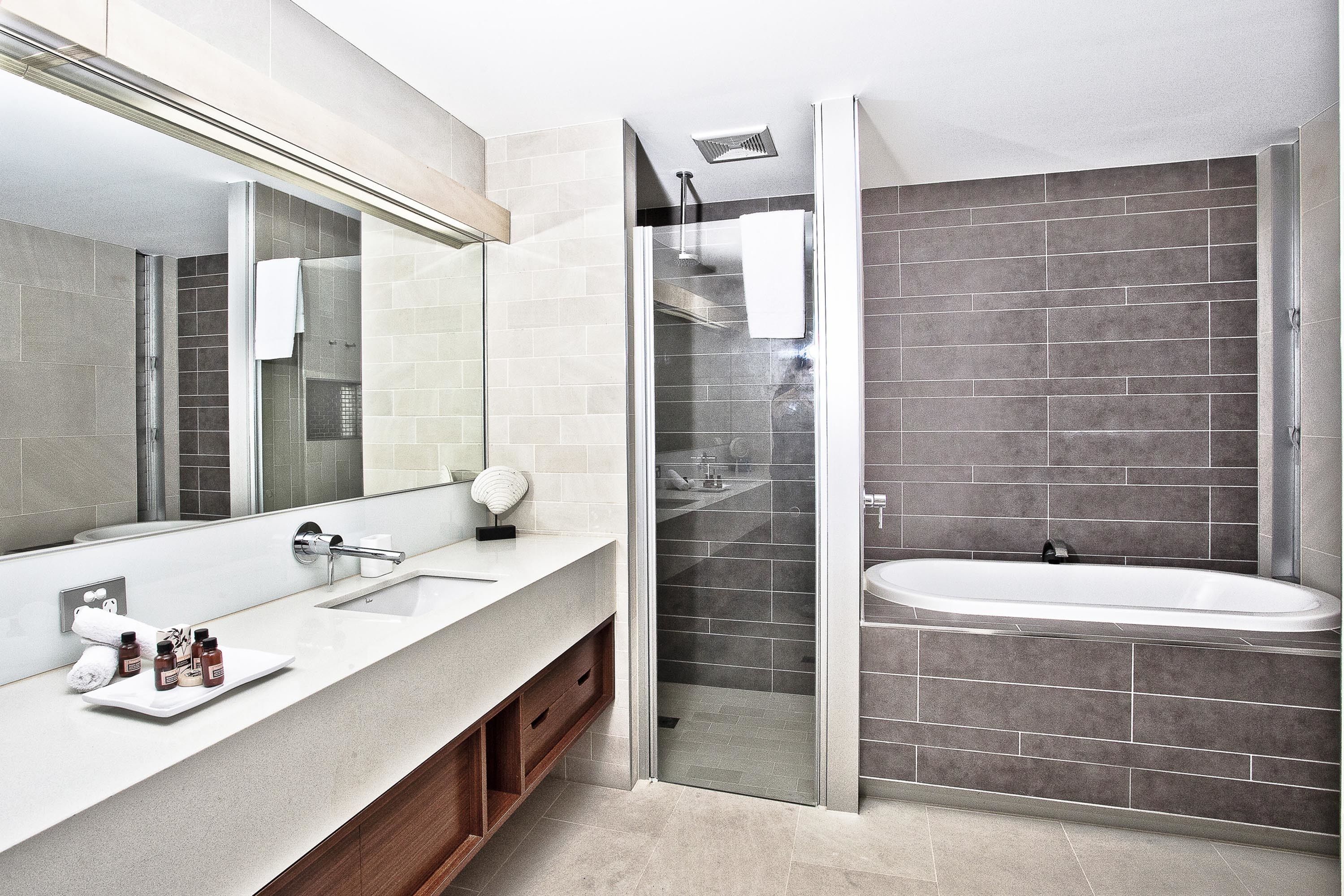 Un baño moderno con un espejo grande, un lavamanos blanco, una ducha con mampara de vidrio y una bañera.