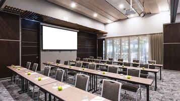 A conference room with long tables, chairs, a projector screen, and a large window.