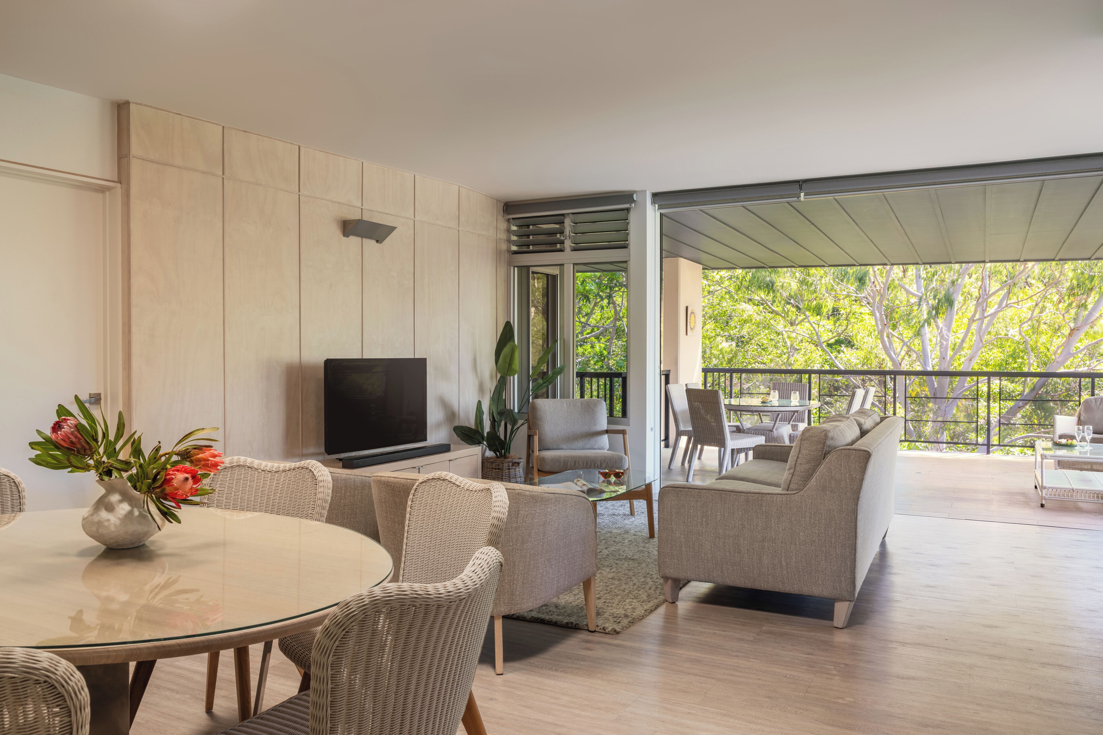 A modern living room with a TV, wicker furniture, a dining table, and a balcony with outdoor seating.