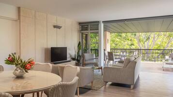 A modern living room with a TV, wicker furniture, a dining table, and a balcony with outdoor seating.