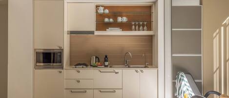 Cocina compacta con microondas, pileta y estantes superiores.
