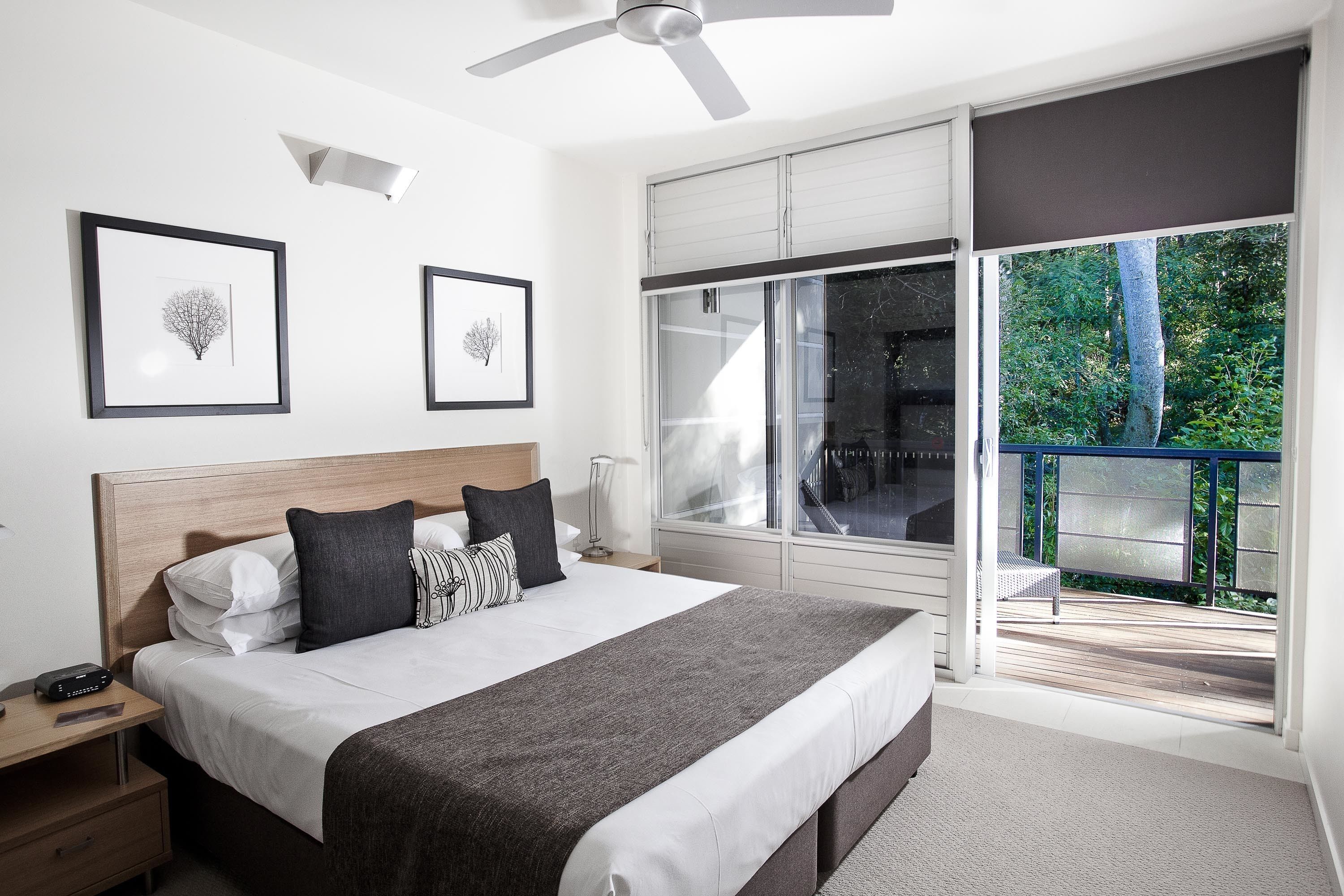 A modern bedroom with a large bed, a ceiling fan, and a balcony with a view of greenery.