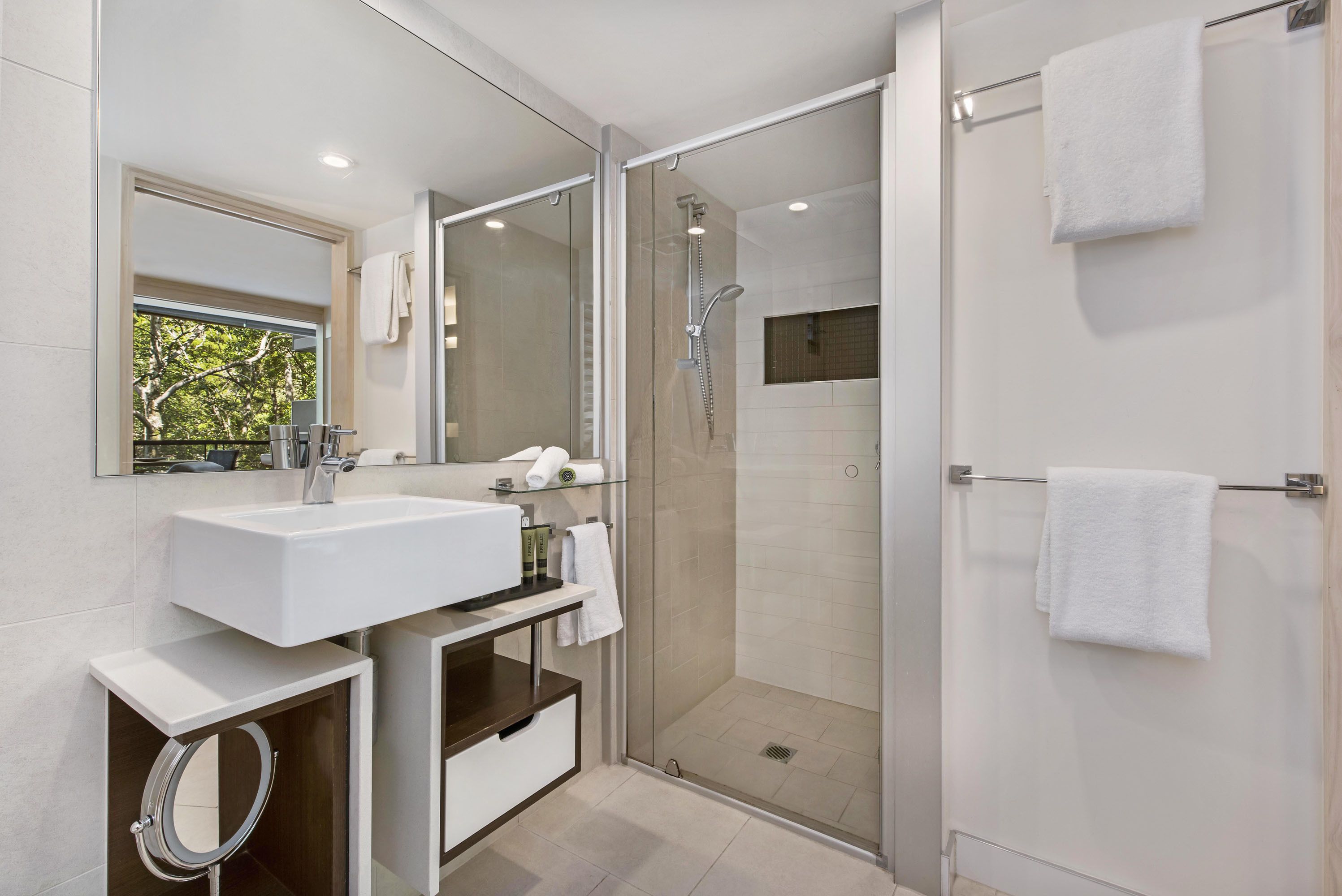 A modern bathroom with a glass-enclosed shower, a large mirror, and a white sink.