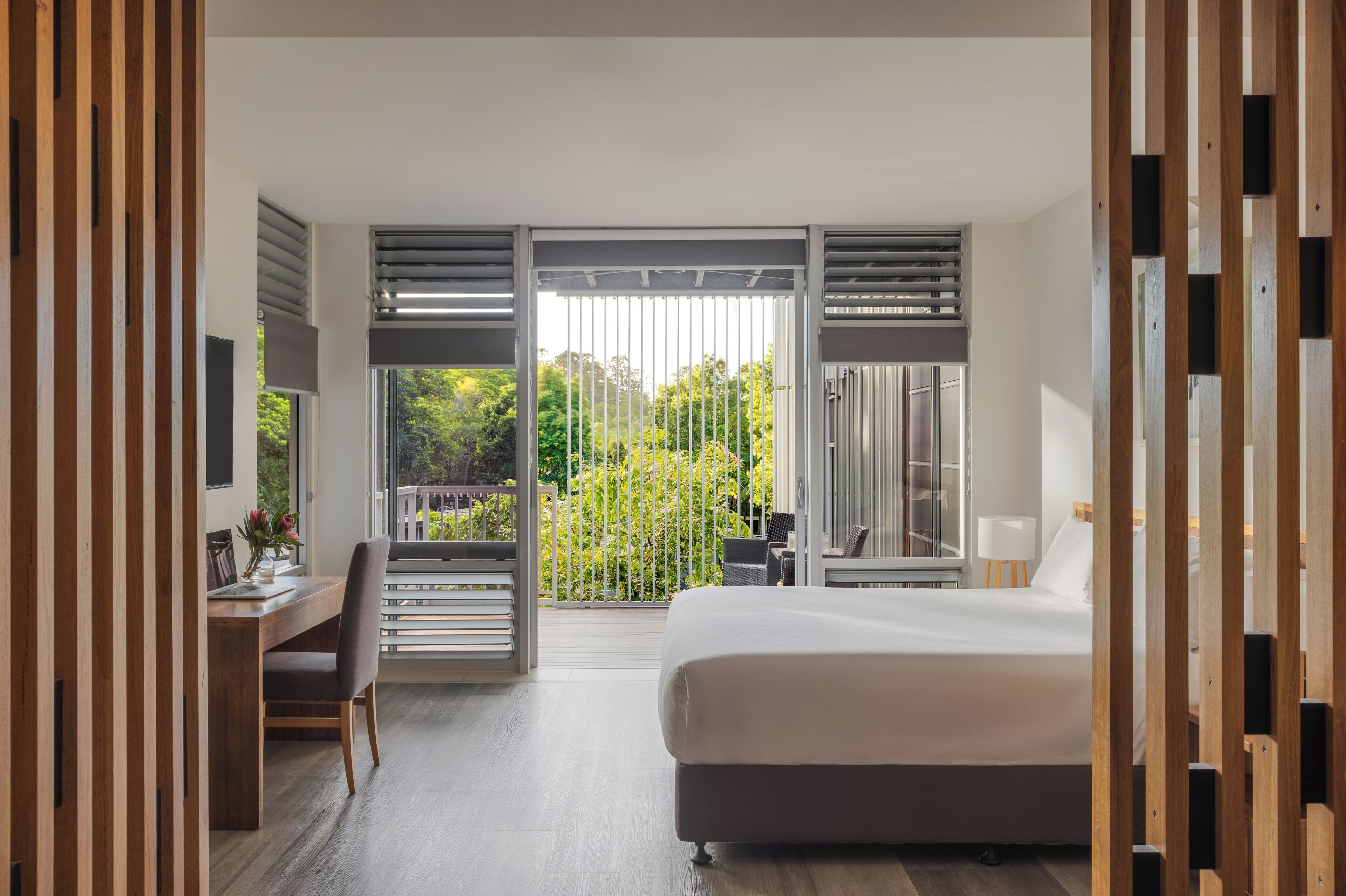Un dormitorio con cama, escritorio y silla, un balcón con vista a zonas verdes y un ventanal corredero.
