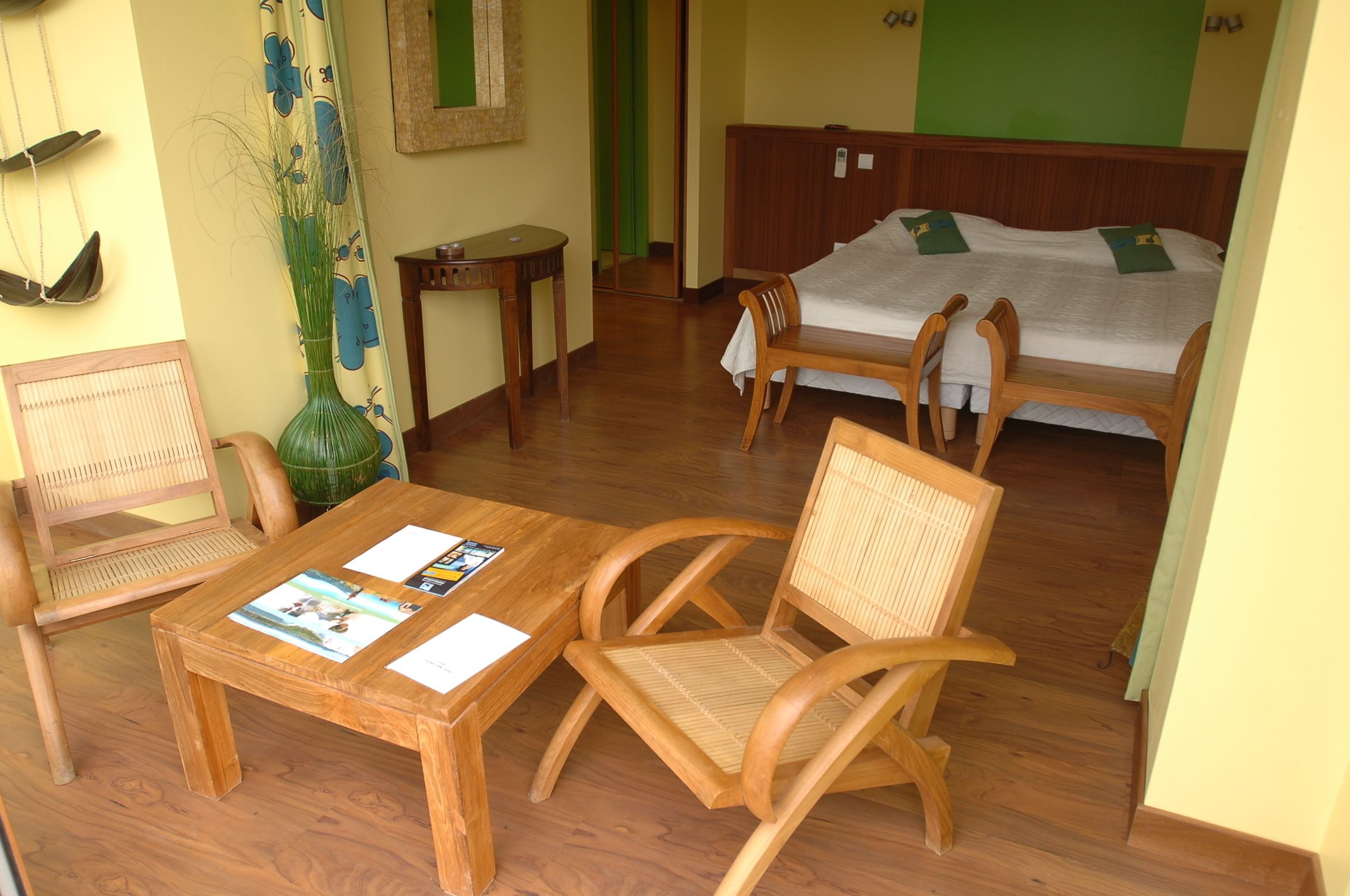 A room with a wooden table, two chairs, a bed, and a mirror on the wall.