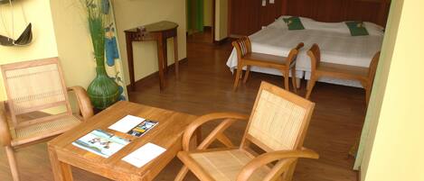 A room with a wooden table, two chairs, a bed, and a mirror on the wall.