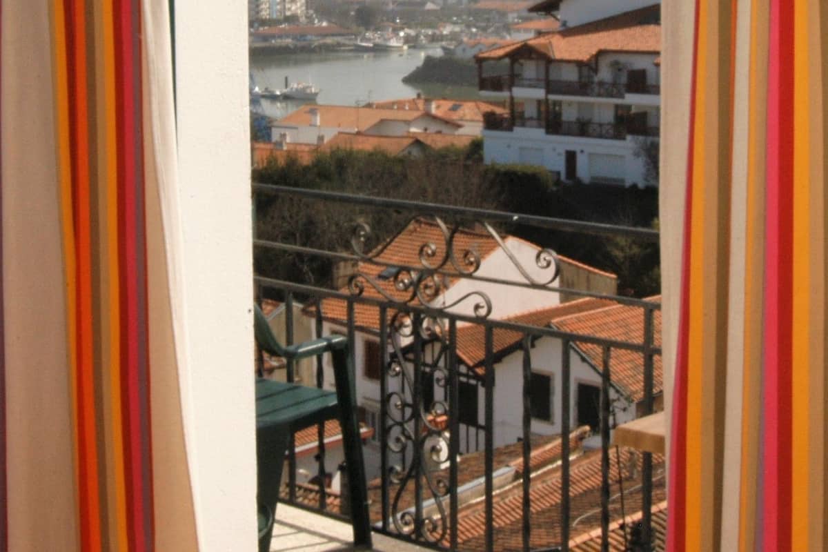 Een balkon met uitzicht op een rivier, gebouwen en een verafgelegen stadsgezicht.