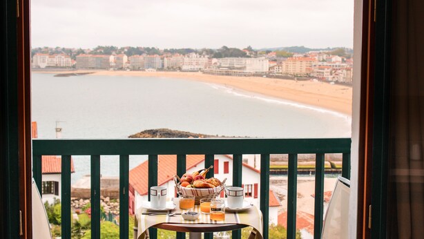 Un balcon avec une table préparée pour le petit-déjeuner, donnant sur une plage et des bâtiments.