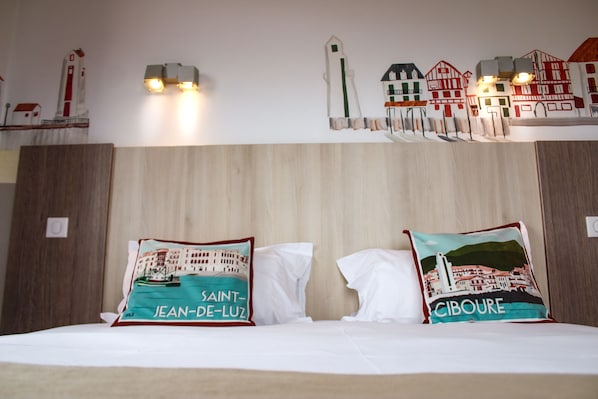 Quarto de hotel com cabeceira de madeira, duas almofadas com estampas de paisagem urbana e luminária fixada na parede.