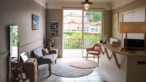 Un salon avec un canapé, des fauteuils, un téléviseur et un balcon donnant sur des immeubles.
