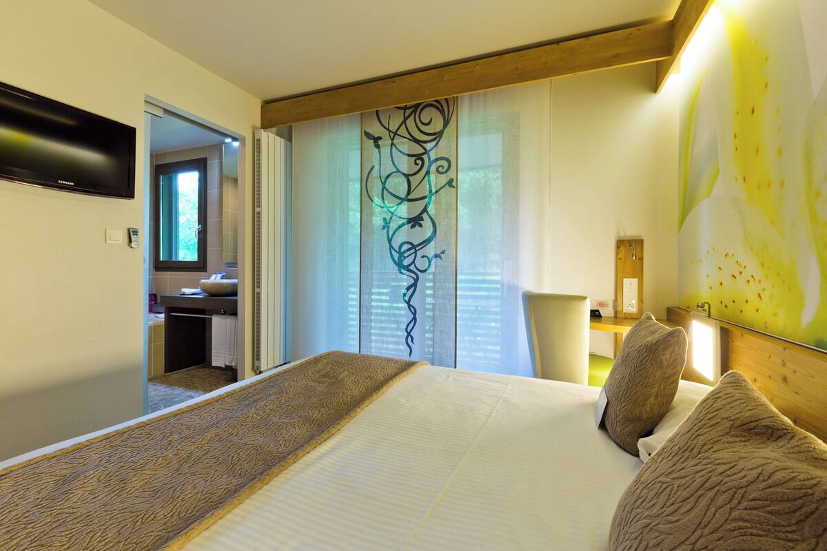 Une chambre d’hôtel avec un lit, un téléviseur fixé au mur, une salle de bain visible à travers une porte ouverte et un élément décoratif mural.
