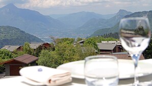 A table with a wine glass and a folded napkin, overlooking a mountainous landscape with houses.