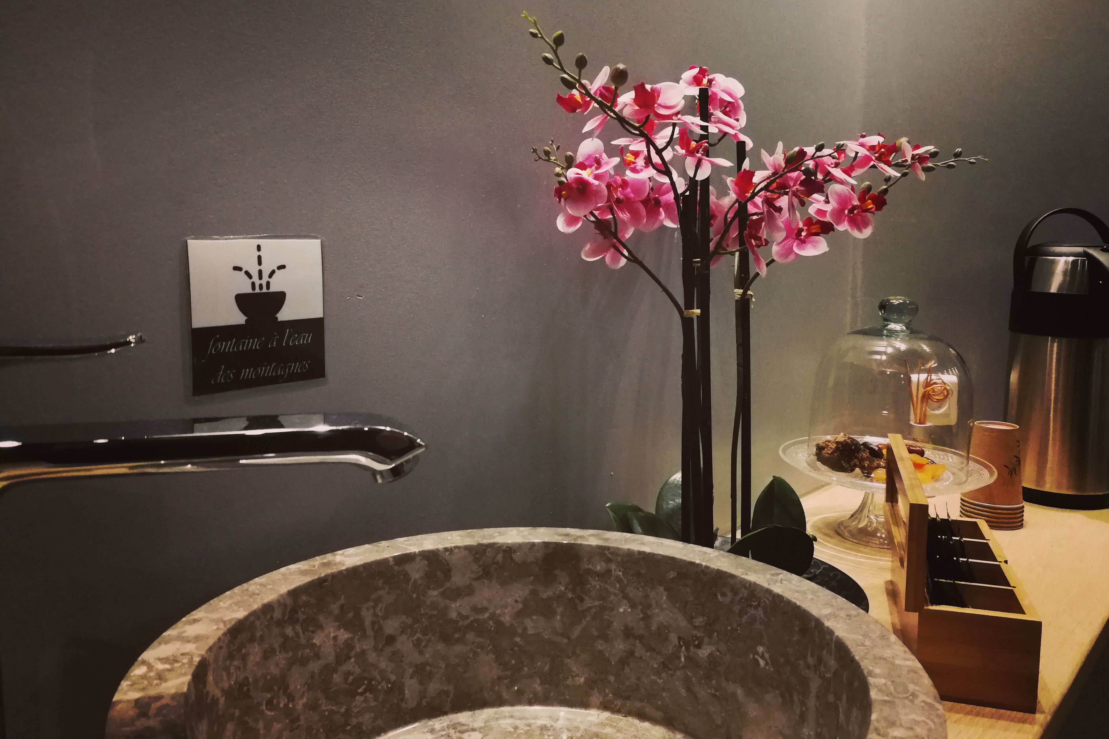 A bathroom with a stone sink, a glass enclosure for toiletries, and a sign with a potted plant.