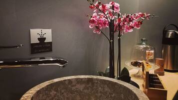 A bathroom with a stone sink, a glass enclosure for toiletries, and a sign with a potted plant.