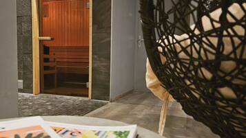 A room with a wooden door leading to a sauna area, a grey wall, and a woven chair.