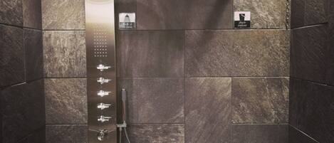 A modern shower with a vertical rain showerhead, a wooden bucket, and a control panel.