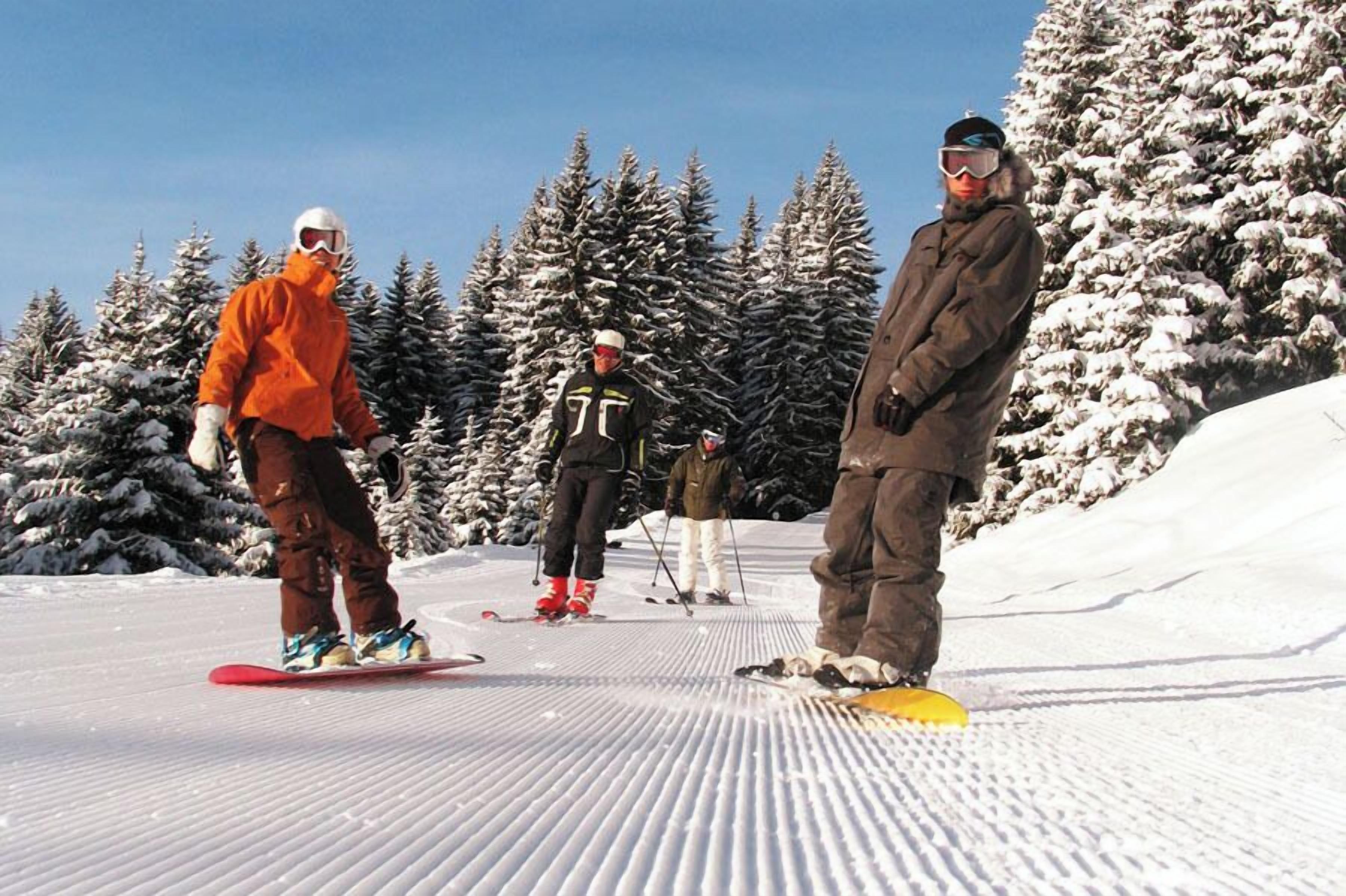 A group of people on snowboards on a snowy slope with trees in the background.