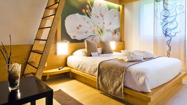 A bedroom with a wooden ceiling, a bed with white linens, a nightstand, a lamp, and a painting of flowers.