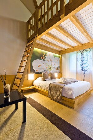 Une chambre avec un plafond en bois, un lit recouvert de draps blancs, une table de chevet, une lampe et un tableau représentant des fleurs.