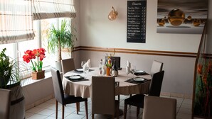 A dining area with a round table set for four, surrounded by chairs. There is a menu board on the wall to the right and a painting above it. - Hotel La Vraine (Gironcourt-sur-Vraine)