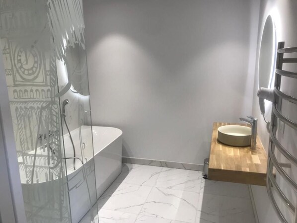 Un baño moderno con ducha envuelta en vidrio, una bañera independiente y un tocador de madera con lavamanos.
