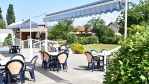 An outdoor seating area with tables and chairs, a covered patio, and a view of the surrounding landscape. - Hotel La Vraine (Gironcourt-sur-Vraine)