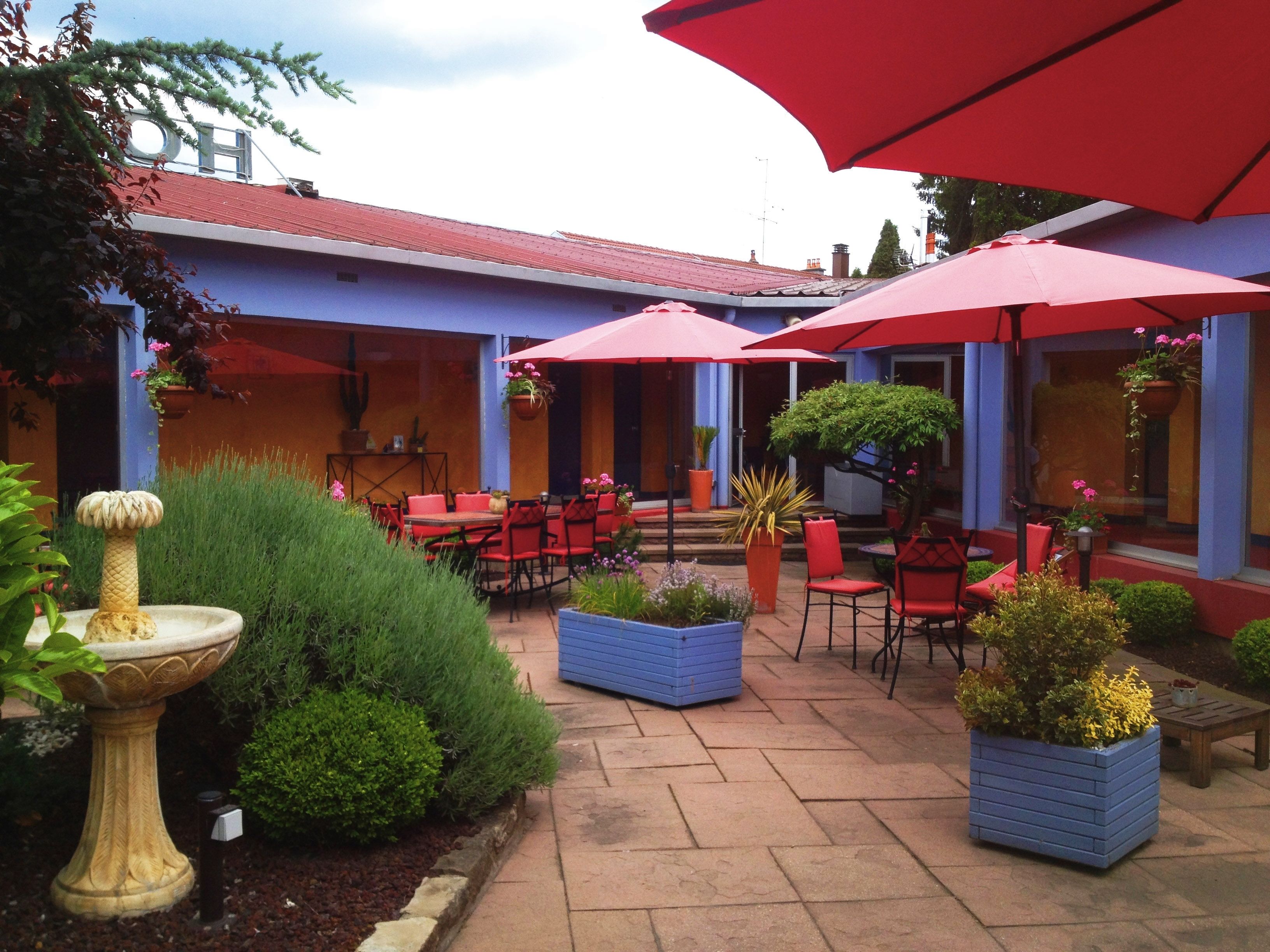 An outdoor patio with red umbrellas, red chairs, and blue planters.