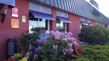 A hotel with a red facade, a sign indicating a handicap accessible entrance, and a variety of flowering plants in the front yard.