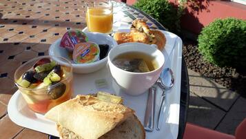 A tray with a sandwich, soup, a glass of juice, and a fruit cup on a tiled table outdoors.
