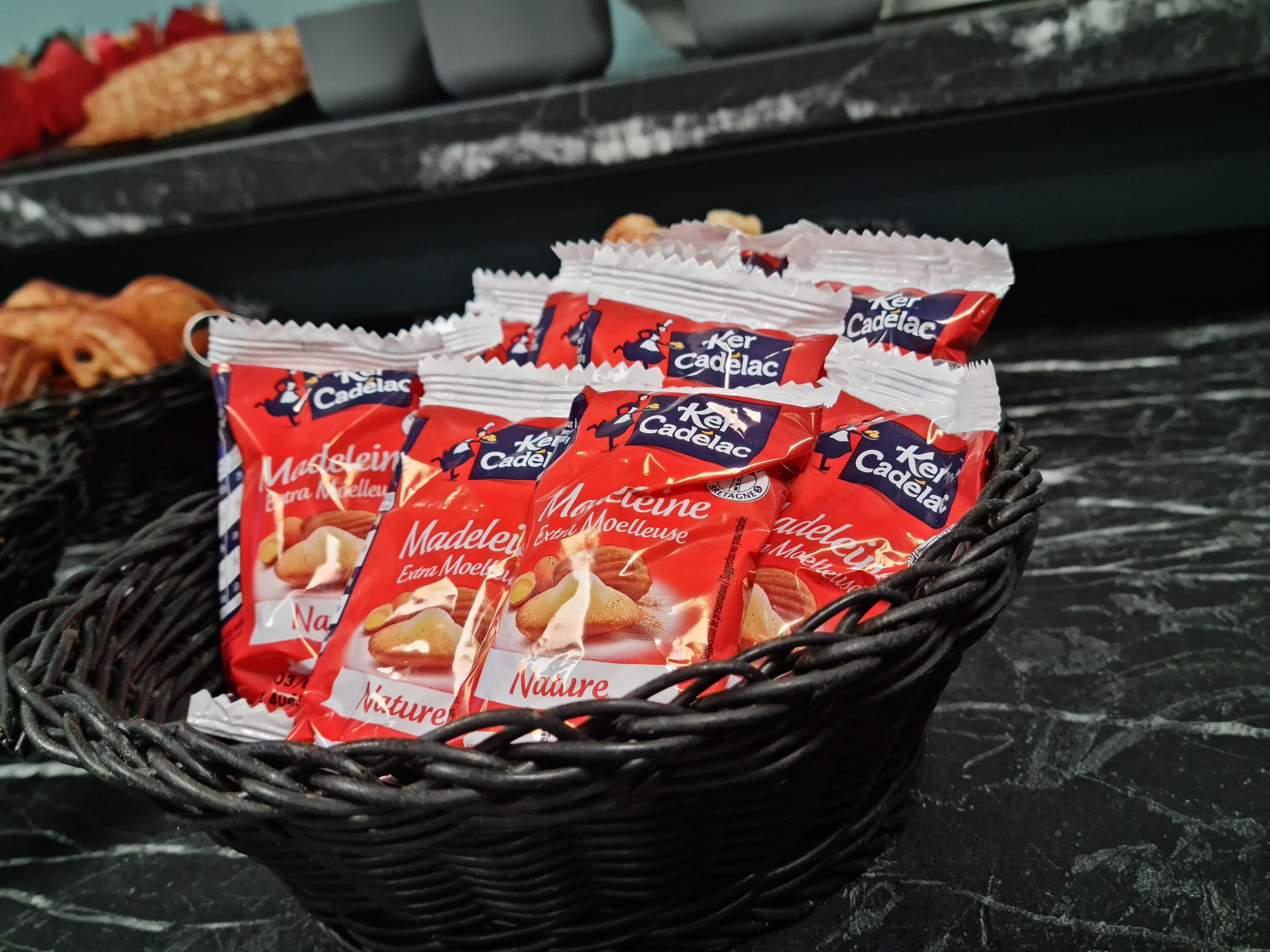 Una cesta de mimbre con varios paquetes rojos y blancos de aperitivos, probablemente con pretzels, sobre una superficie oscura.