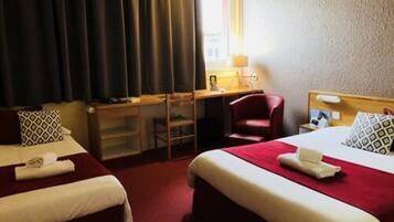 Et hotelværelse med to senge, et skrivebord, en stol og et vindue med gardiner.